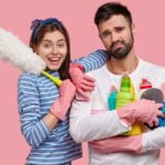 glad attractive woman has toothy smile leans shoulder handsome displeased man holds brush 1