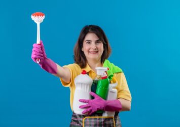 middle aged woman wearing apron rubber gloves holding cleaning supplies scrubbing brush 1