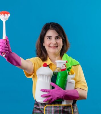 middle aged woman wearing apron rubber gloves holding cleaning supplies scrubbing brush 1